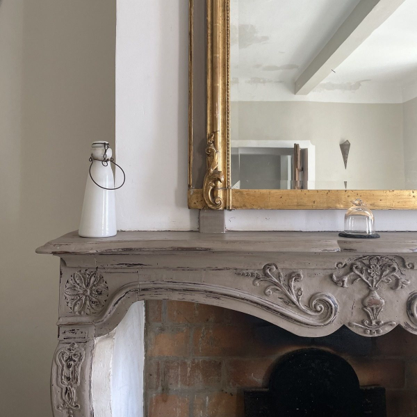 An elegant gilded mirror and a carved fireplace adorn this charming antique living room.