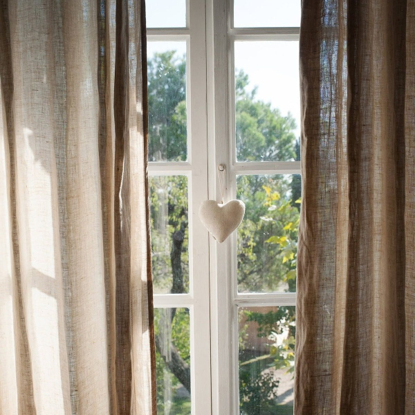 Beige linen curtain in front of a window with a felt heart attached.