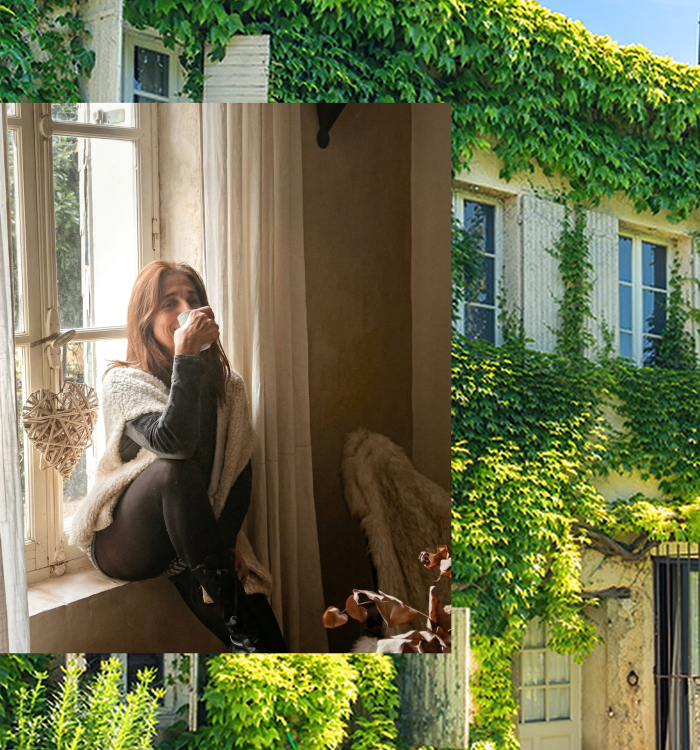 Une femme savoure une boisson près d'une fenêtre ornée de lierre, dans un décor champêtre.